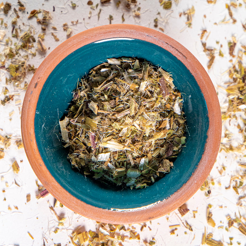 Blessed Thistle herb in blue clay bowl with white background and herb surrounding.