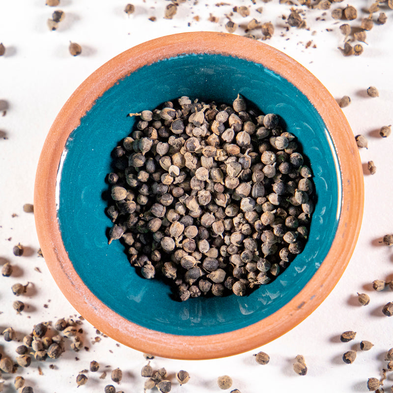 Chaste Tree Berry herb in blue clay bowl with white background and herb surrounding.