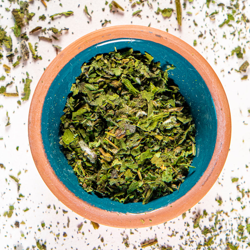 Comfrey herb in blue clay bowl with white background and herb surrounding.