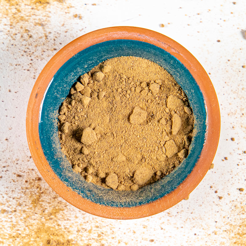 Devil's Claw Powder herb in blue clay bowl with white background and herb surrounding.