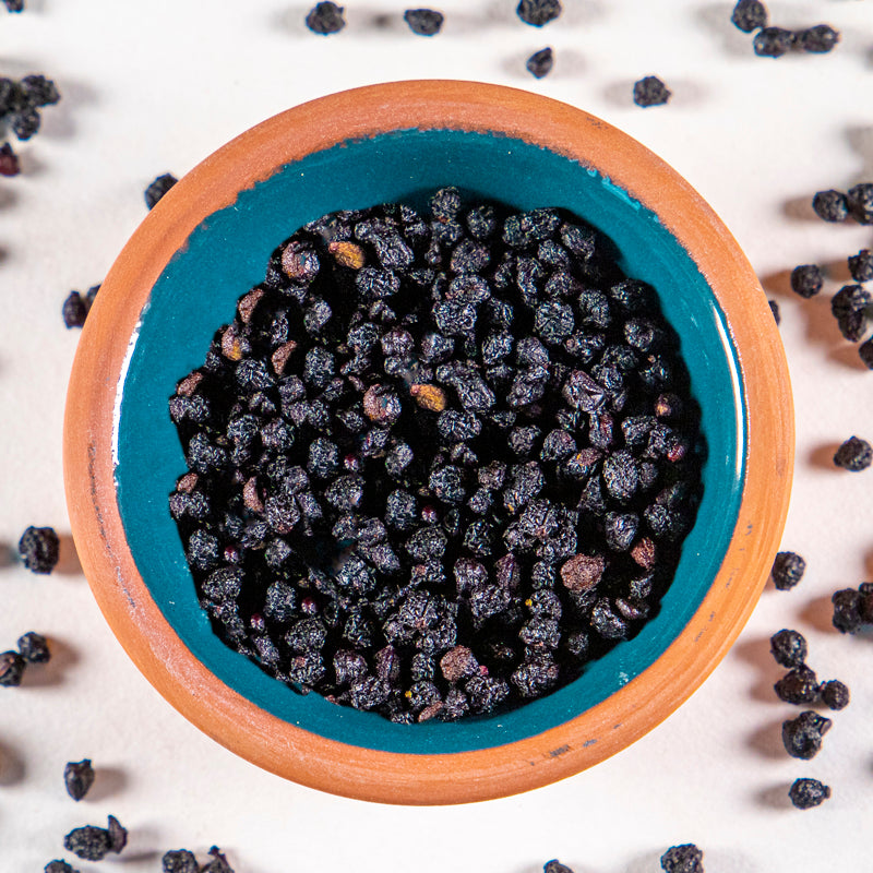 Elderberry herb in blue clay bowl with white background and herb surrounding.