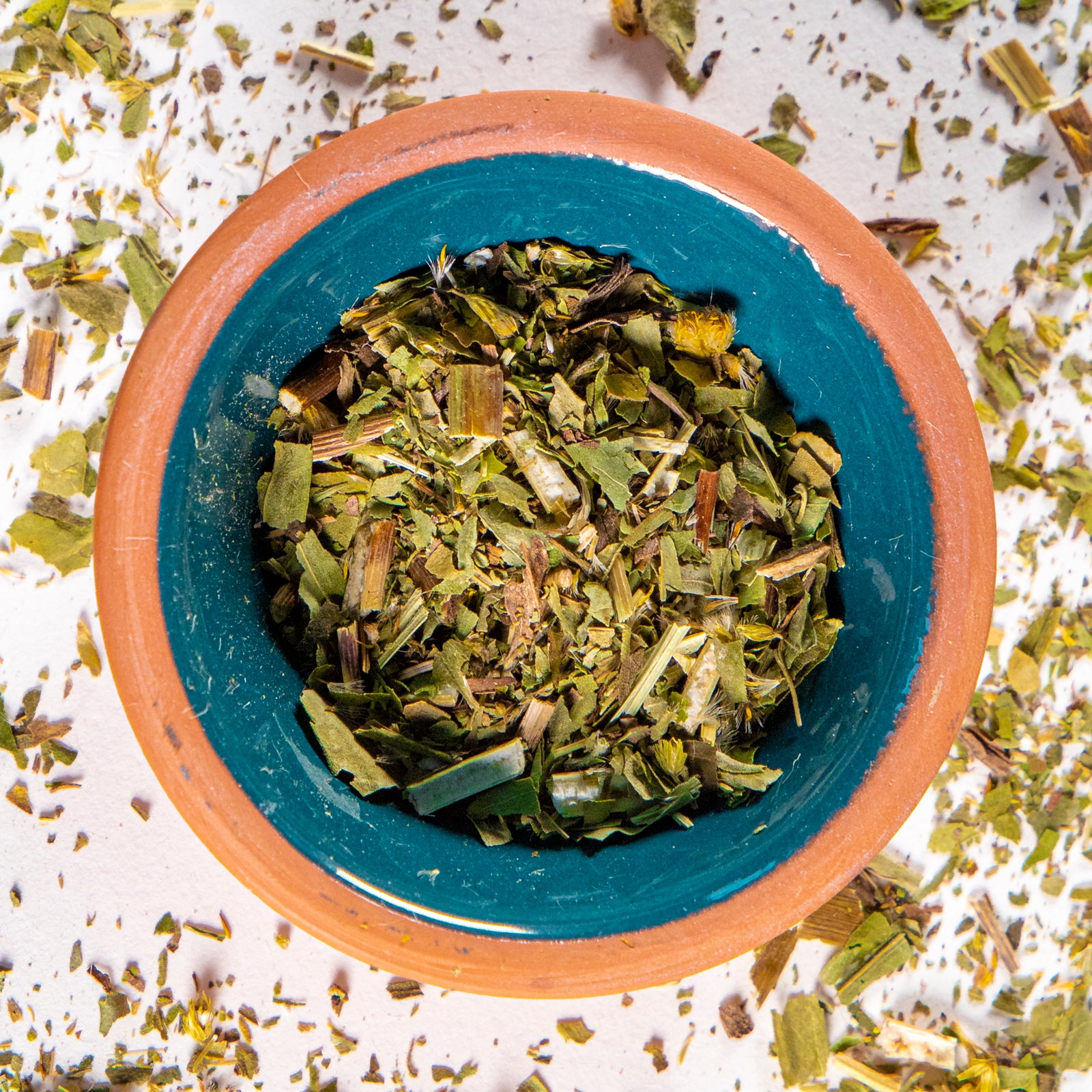 Golden herb in blue clay bowl with white background and herb surrounding.