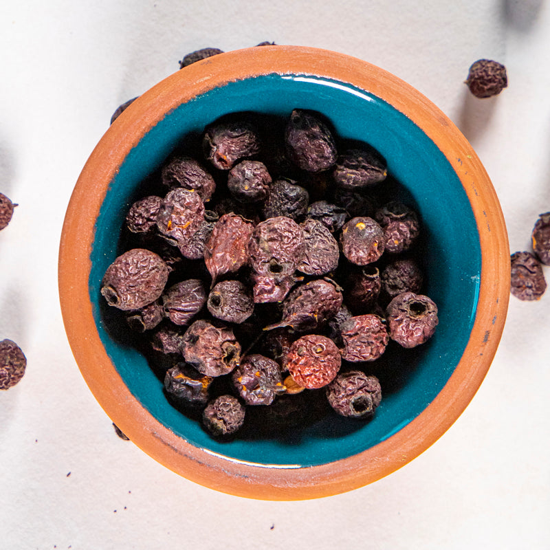Hawthorn Berries in blue clay bowl with white background and herb surrounding.