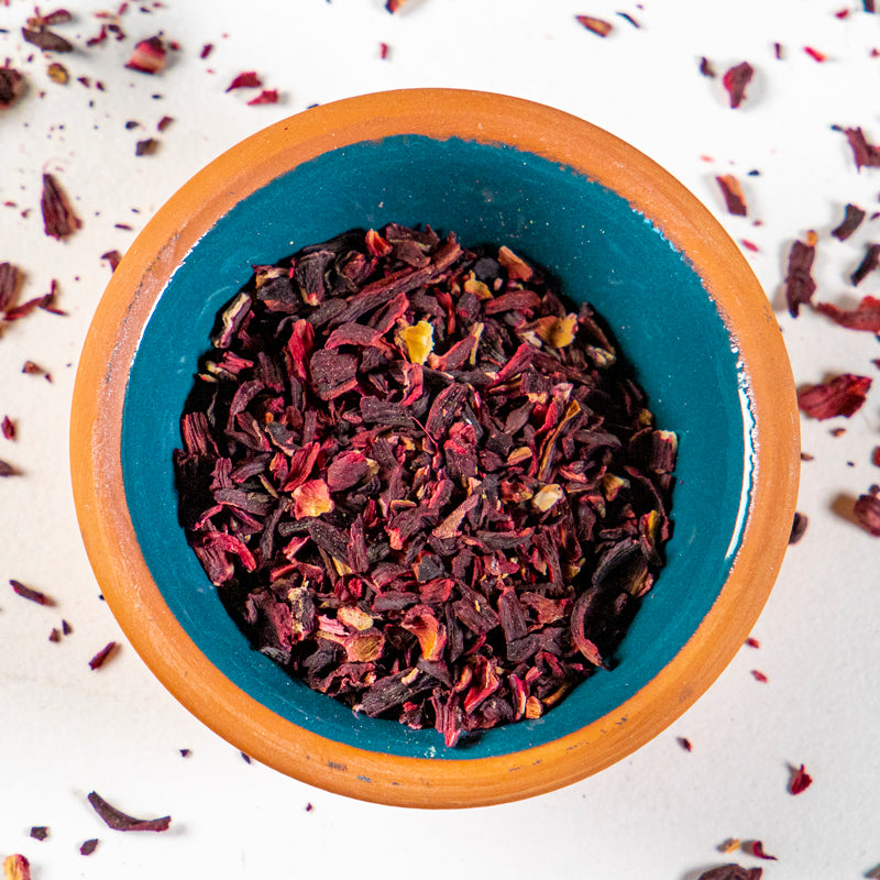 Hibiscus Flowers herb in blue clay bowl with white background and herb surrounding.