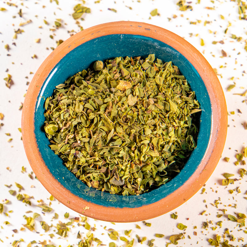Oregano Leaf herb in blue clay bowl with white background and herb surrounding.