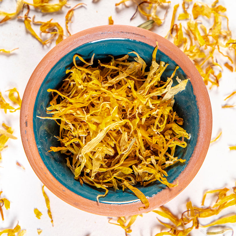 Calendula Flowers herb in blue clay bowl with white background and herb surrounding.